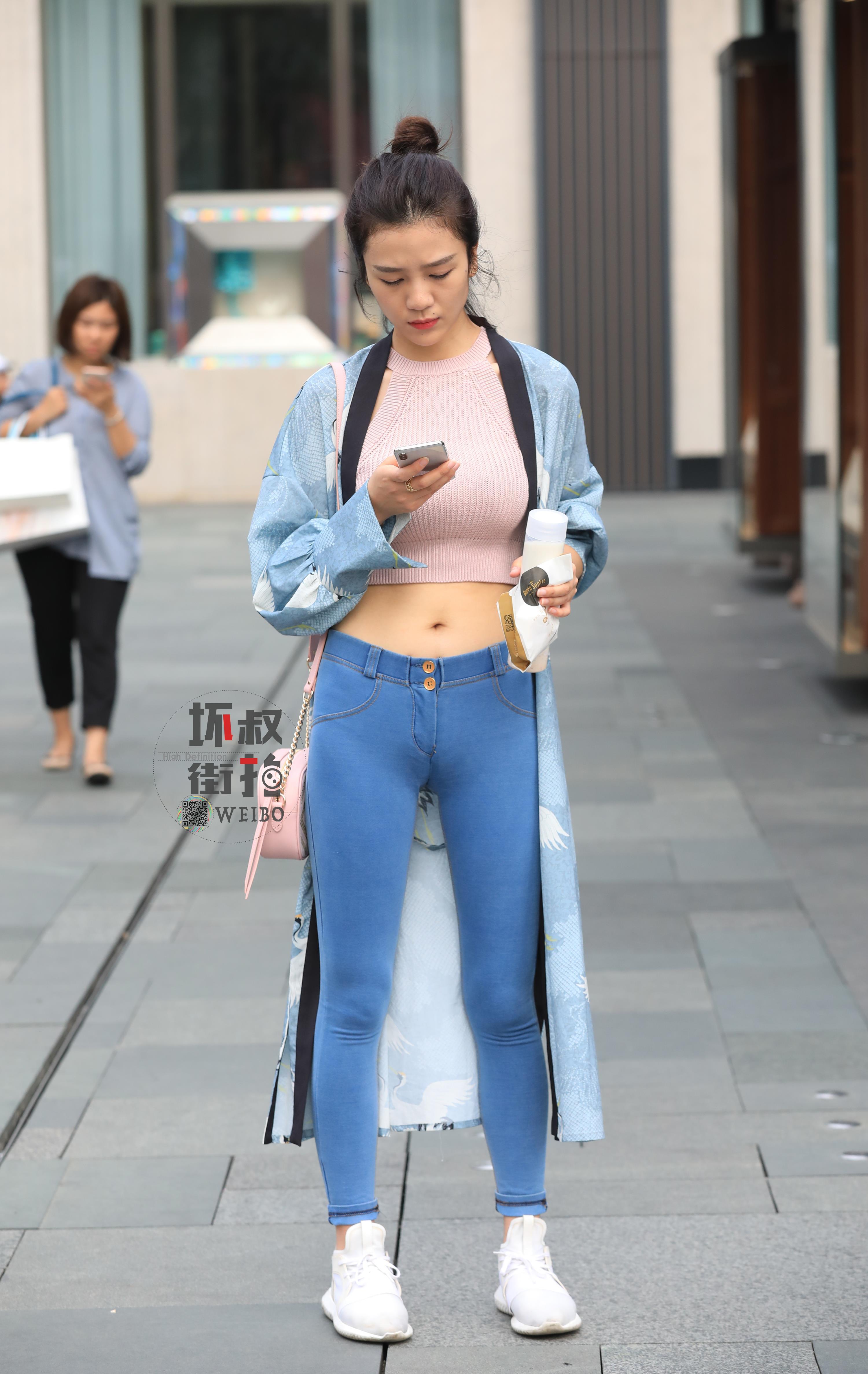 购物街边走边玩手机的性感美女 粉色镂空上衣加紧身牛仔裤,